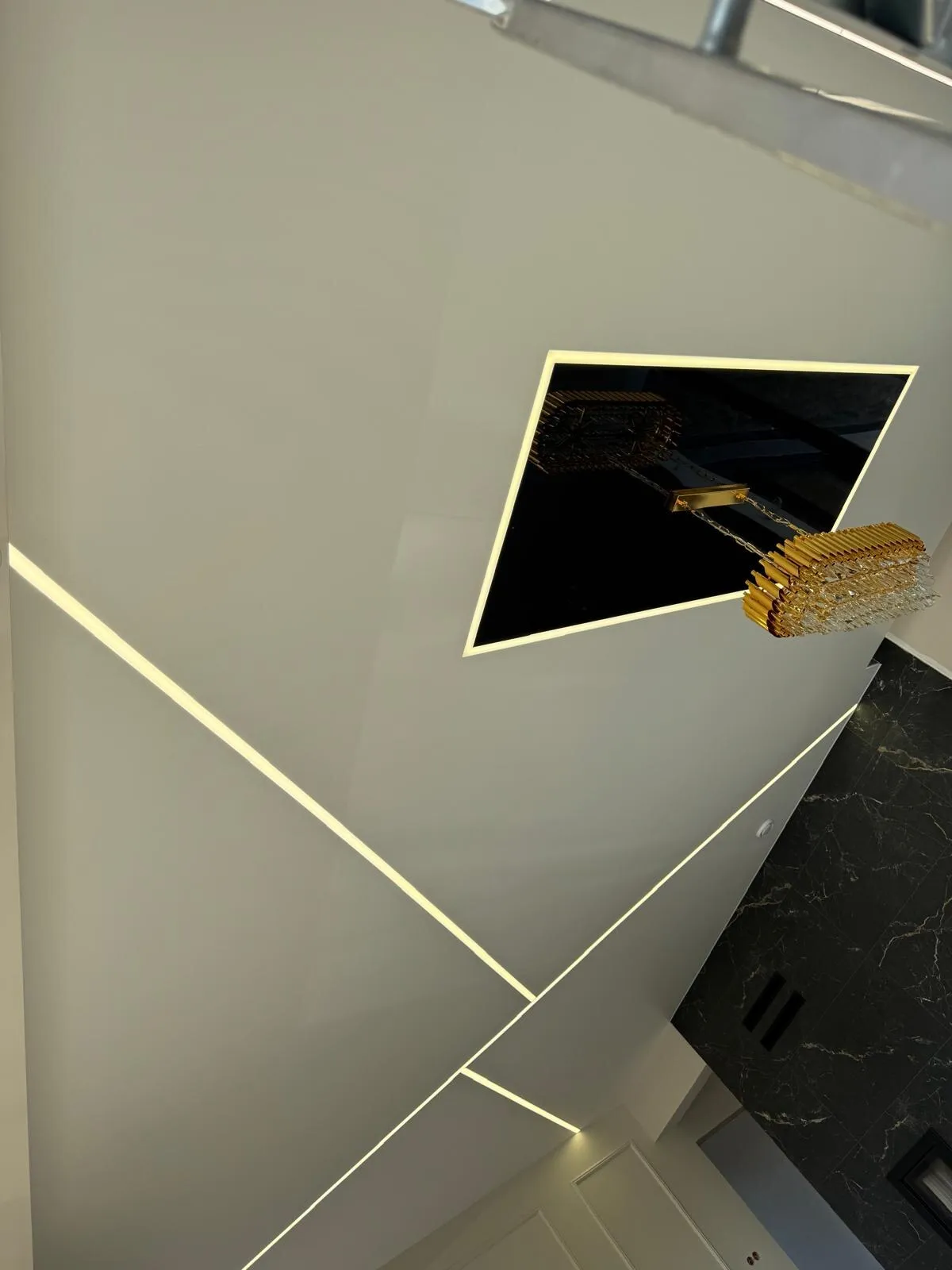 Sufit z białymi liniami LED i czarną lustrzaną wstawką z żyrandolem